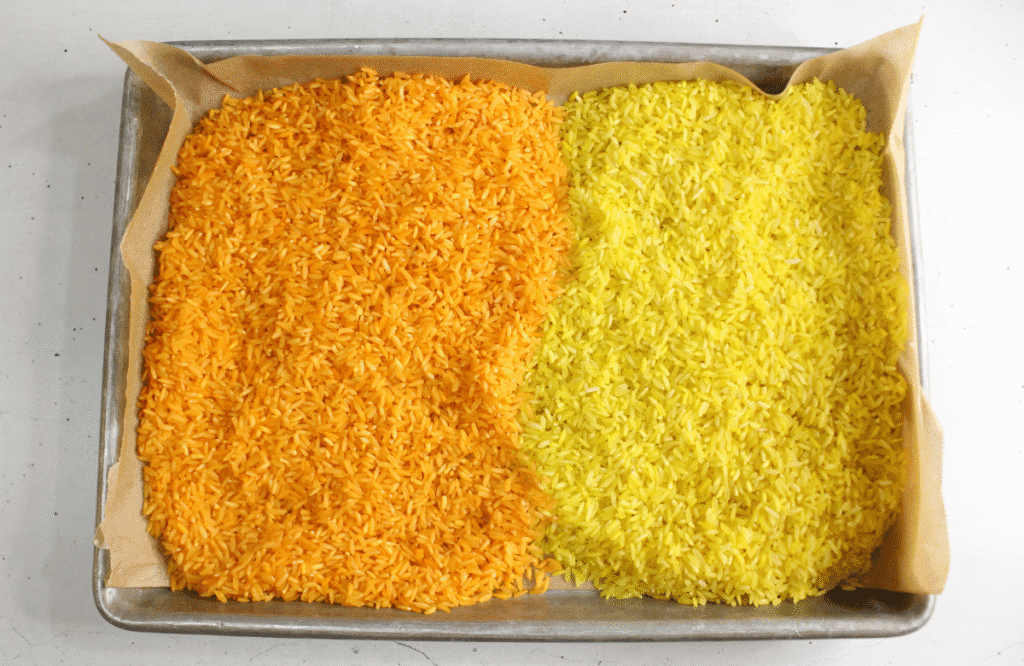 Bright orange and yellow dyed rice drying on a parchment-lined baking tray for a fall-themed candy corn sensory bin for toddlers. This step is part of a fun DIY Halloween sensory activity that supports early childhood development, perfect for fall sensory bins in preschool classrooms.

