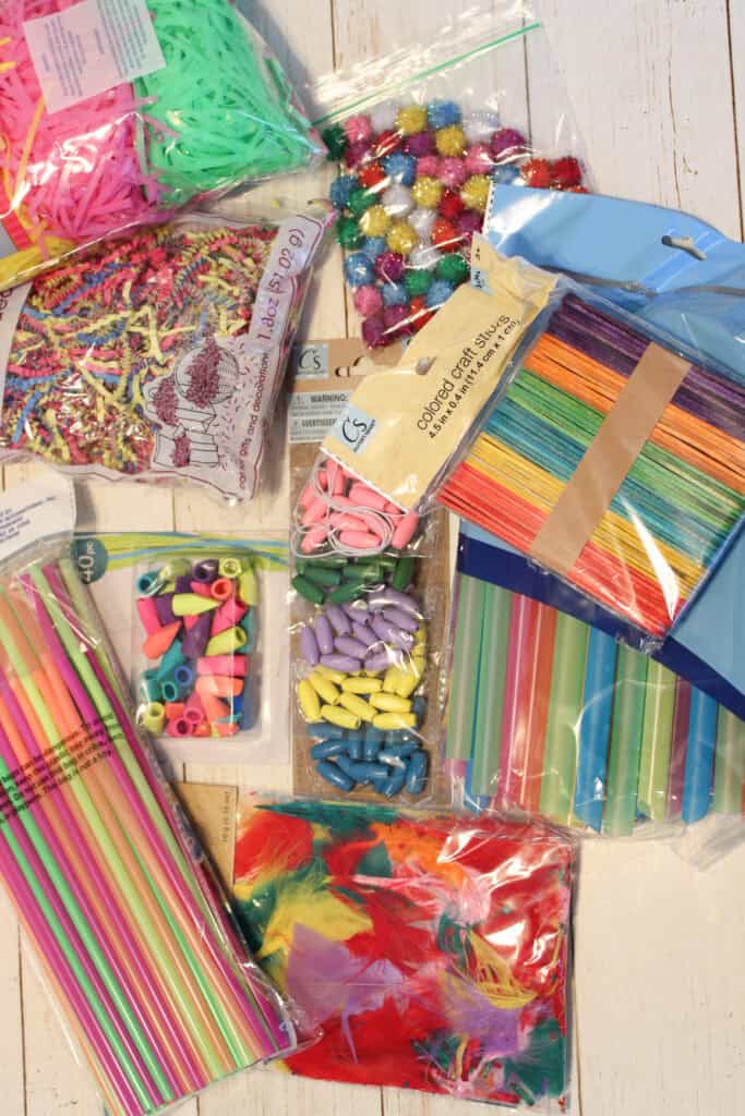 Supplies You’ll Need for a Non-food Sensory Bin
Supplies for a non-food sensory bin for toddlers and preschoolers: multicolored bendable straws, bubble tea straws, Easter basket grass, craft sticks, pom-poms, beads, mini erasers, feathers, decorative crinkled paper, plastic sensory bin, tongs, cups, scoops, and spoon for engaging hands-on sensory play.